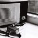 Black and white still life featuring a retro radio, glasses, and cigarette pack by a window.